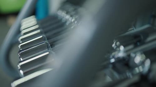 Sideways reveal of shiny metallic dumbbell rack at indoor gym facility