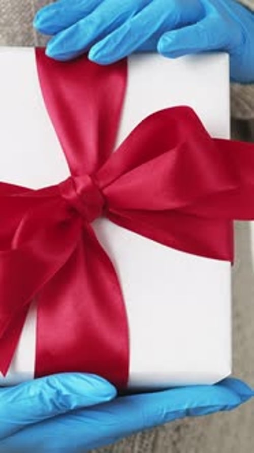 Gift with Red Bow in Blue-Gloved Hands
