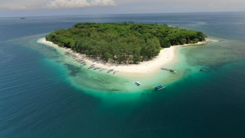 Aerial descending push in shot to a tropical island in the middle of the ocean. White sand beach wit