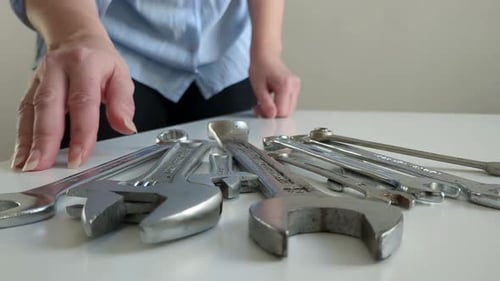 Woman picking up small spanner, multiple wrench tools on table