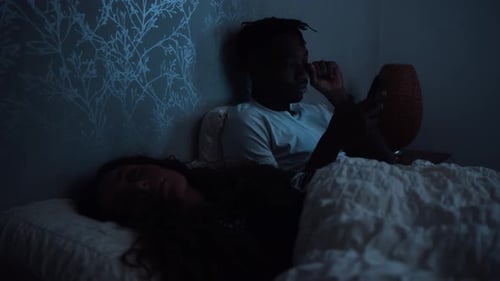 Concentration entre une femme endormie et un homme qui reste éveillé en utilisant un téléphone intelligent tard dans la nuit