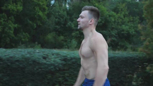 Close Up of Young Muscular Man Sprinting Fast Along Trail Near Forest at Summer Day
