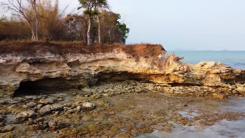 Aerial: Fly over a rocky cliff on the ocean. Traveler sits and enjoys beautiful sea view, on the sea