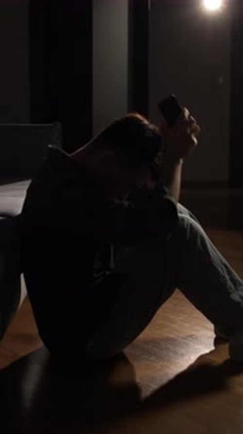 Vertical Video Man Covering His Face with Hands Sitting Alone on a Dark Room Floor with a Minimal
