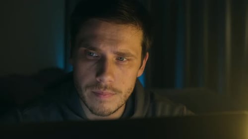 Junger Mann sitzt am späten Abend gebeugt über dem Laptop im Büro