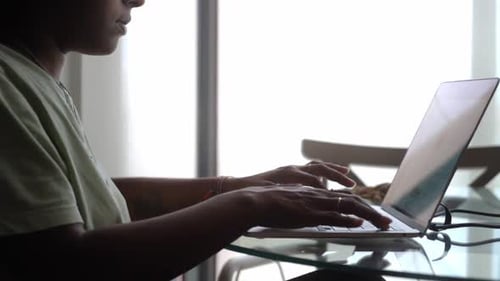 Concentrated African American Woman Working Using Laptop Sitting By a Window at Home