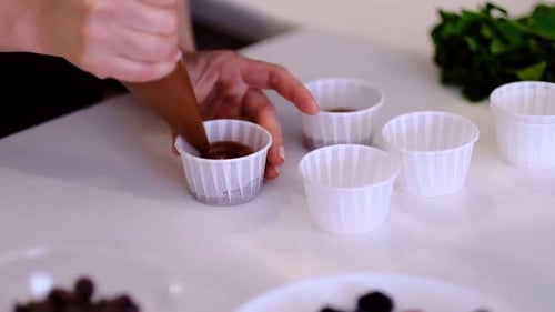 Nahaufnahme weiblicher Hände legt die Sahne aus dem Gebäckbeutel auf Schokoladen-Cupcakes, junge Frau