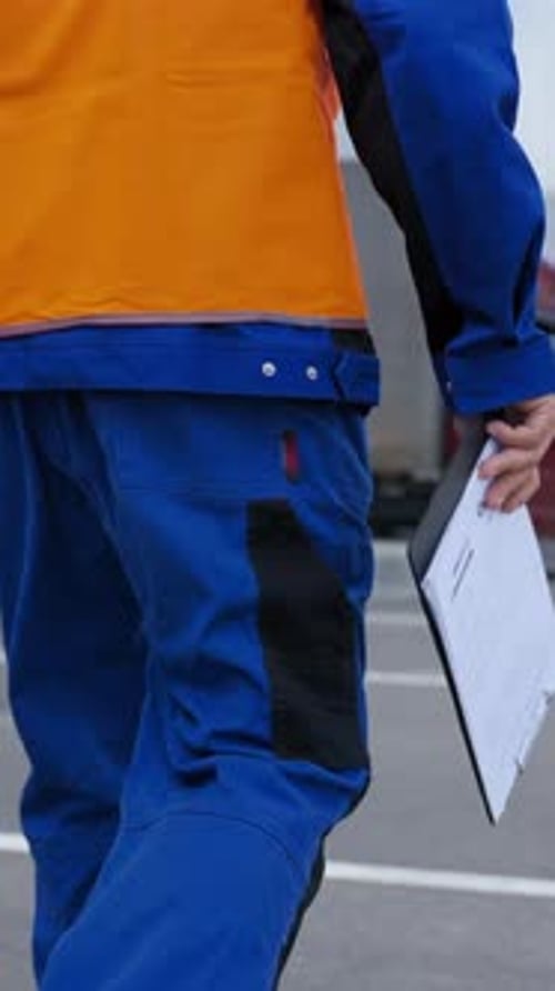 Vertical of Engineer Walks Towards Truck Holding Clipboard with Plan