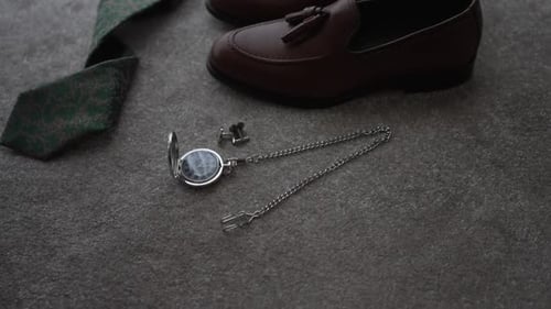 Close-up of groom's wedding accessories: brown loafers, green tie, silver pocket watch, and cufflink