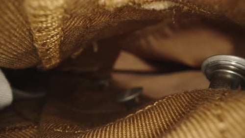 The camera glides through the zipper of the brown jeans with buttons. Dolly slider extreme close-up.