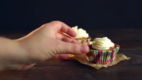 Hand Reaches for Cupcake with Cream Frosting