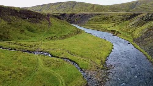Aerial drone view of a river winding through a narrow canyon surrounded by grassy volcanic hills and