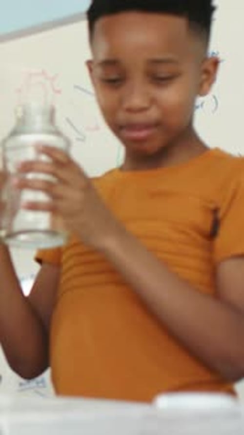 Vertical video: Camera shifting orange-shirt kid turning jar lid exploring in class near whiteboard