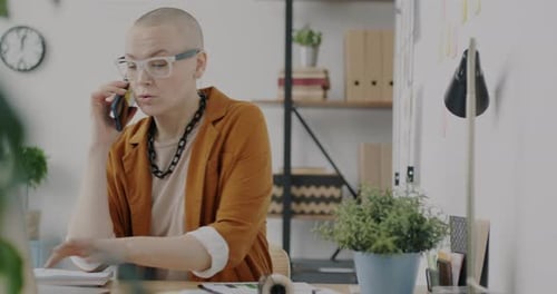 Portrait of Stylish Businesswoman Speaking on Mobile Phone and Using Laptop at Desk in Office