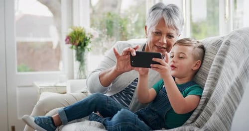 Grandmother and Grandson Relaxing Indoors While Using Phone