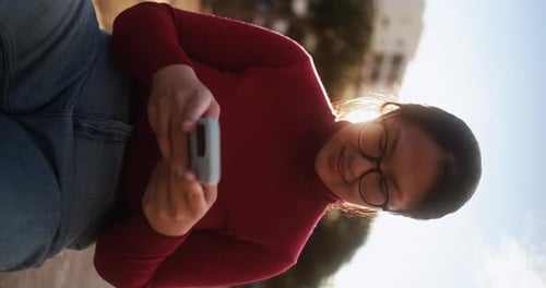 Woman uses phone outside in sunlight, urban setting
