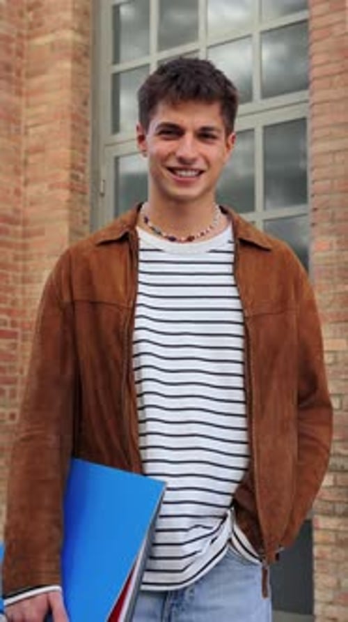 Portrait individuel vertical d'un écolier populaire regardant la caméra debout au lycée réel