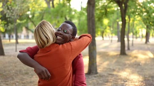 Slow motion video of two happy multiethnic female friends affectionately embracing in a city park