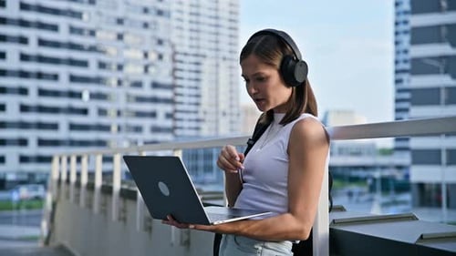 Woman Using Laptop with Headphones in Urban Setting