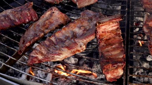 Gegrillte Schweinerippchen auf dem Grill mit Feuerflammen unter dem Grill in Zeitlupe