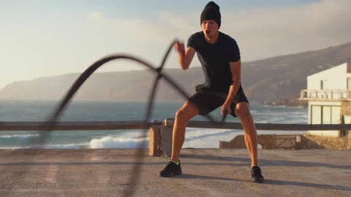Aktives sportliches Männertraining mit Battle Ropes auf der Plattform am Meer