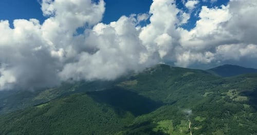 Flying trough white fluffy clouds above green mountain peaks. Beautiful summer sunny day on the high