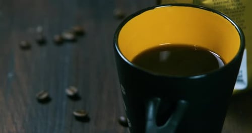 close up shot of a cup of coffee next to a packet of coffee beans and coffe beans on a wooden table