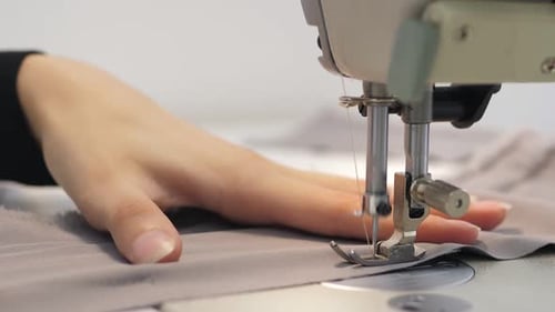 Close Up Slow Video of Woman's Hand Sews Grey Fabric on a Professional Sewing Machine at the