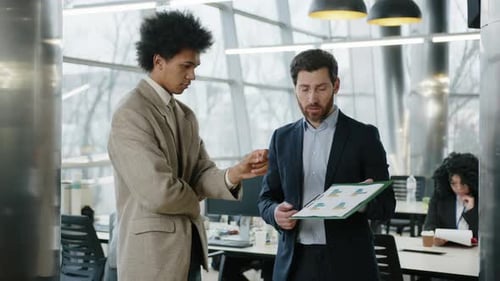 Two Men Discuss Charts in Office