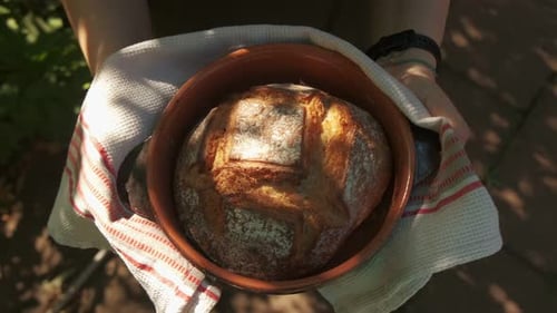 Top orbiting view of a freshly baked round french bread held by a woman baker 4K slow motion