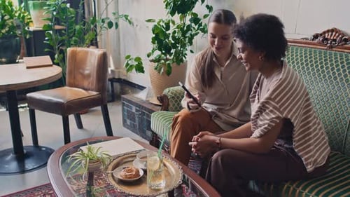 Girlfriends Looking at Photos on Smartphone and Gossiping in Cafe