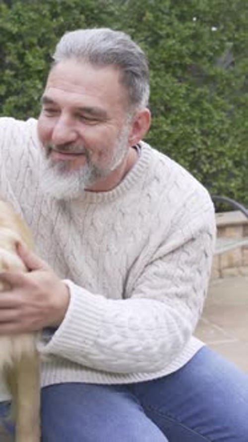 Vertikales Video: Streichelnder goldener Hund mit Tennisball im Mund, Mann in cremefarbenem Pullover auf einem Felsvorsprung