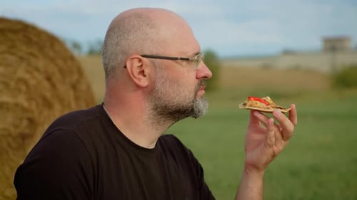 Man Eating Pizza Outdoors in Field Fast Unhealthy Food Male Enjoying Slice of Pizza Amidst Rural