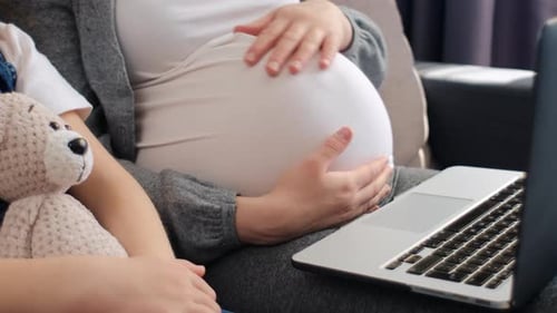Close up of unrecognizable young pregnant mother with little daughter using laptop at home