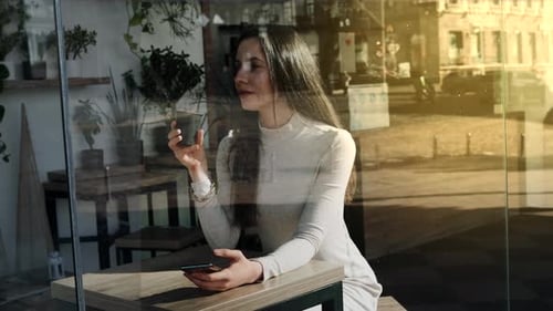 Pretty Young Woman with a Smartphone in Cafe with a Cup of Coffee Smiling