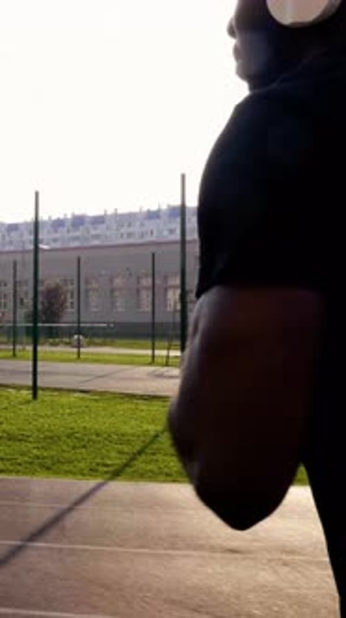 African American Man Jogging Outdoors with Headphones and Smartphone in a Vibrant Green Park