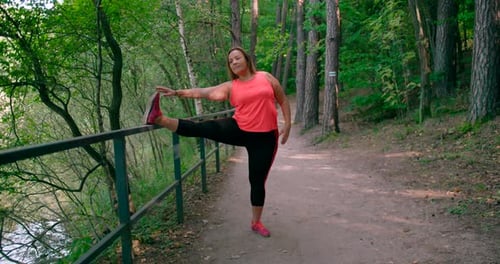 A close-up view of a caucasian lady is in sportswear doing stretching exercises in a park surrounded