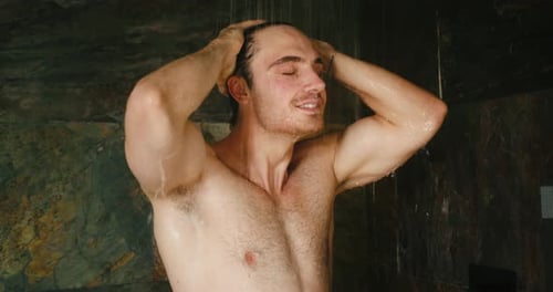 Shirtless Man Enjoys Showering in Stone-Walled Bathroom
