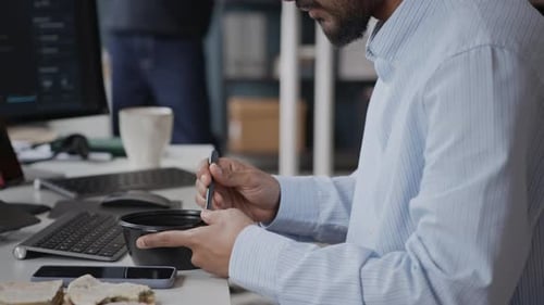 Young Indian Male Developer Eating Lunch at Workstation in front of PC