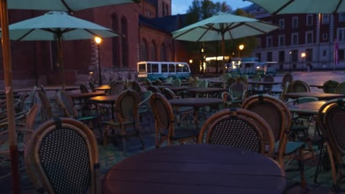 An Evening Scene Captures an Empty Outdoor Cafe with Umbrellas in the City Under the Twilight Sky