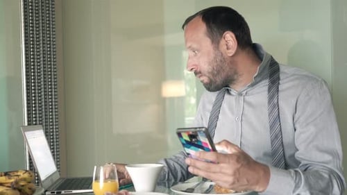 Man Eating Sandwich, Using Phone, Working on Laptop