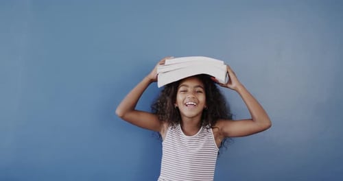 Girl Smiles with Books Balanced on Head