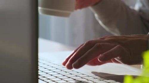 Male Hands Typing Keyboard on Laptop Computer and Drinking Cup of Coffee Man Working Online at Home