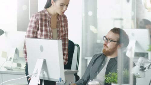In a Busy Office Beautiful Girl Approaches Her Male Colleague Who is Sitting at His Desk and They R