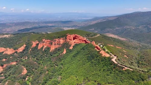Red rock formations sticking out of greenery. Vast scenery of mountainous landscape on sunny day.
