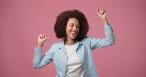 Young African American Woman with Afro Hair Having Fun Smiling and Dancing in Studio Against Pink