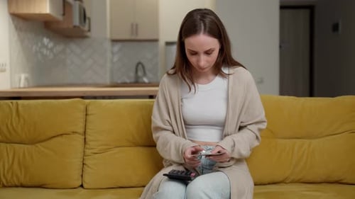 Woman with Money and a Calculator is Sitting on a Yellow Sofa A Concerned Woman with Financial