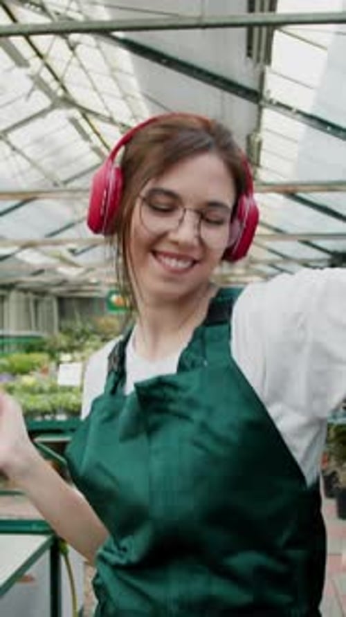 Cheerful Brunette Woman in Glasses Listens to Music in Wireless Red Headphones and Dances in a Green
