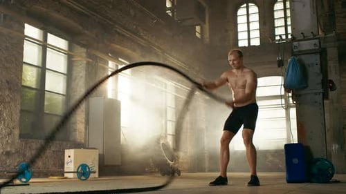 Muscular Shirtless Man in a Gym Exercises with Battle Ropes During Her Cross Fitness Workout High-