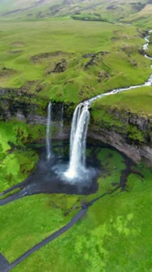 Majestic Waterfall Cascading Down Cliffs Surrounded By Lush Green Landscape in Iceland